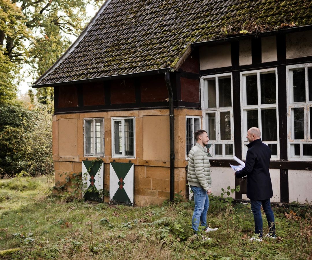 Zwei Personen besichtigen ein älteres Wohnhaus in ruhiger, grüner Umgebung